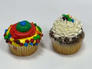 Two cupcakes topped with colorful candies and buttercream